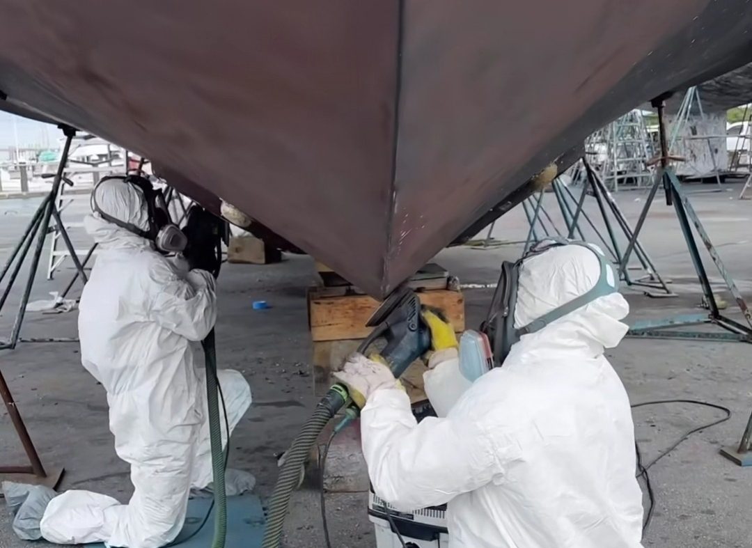 Two men in white suits are applying paint to a boat, showcasing teamwork and attention to detail in their work.